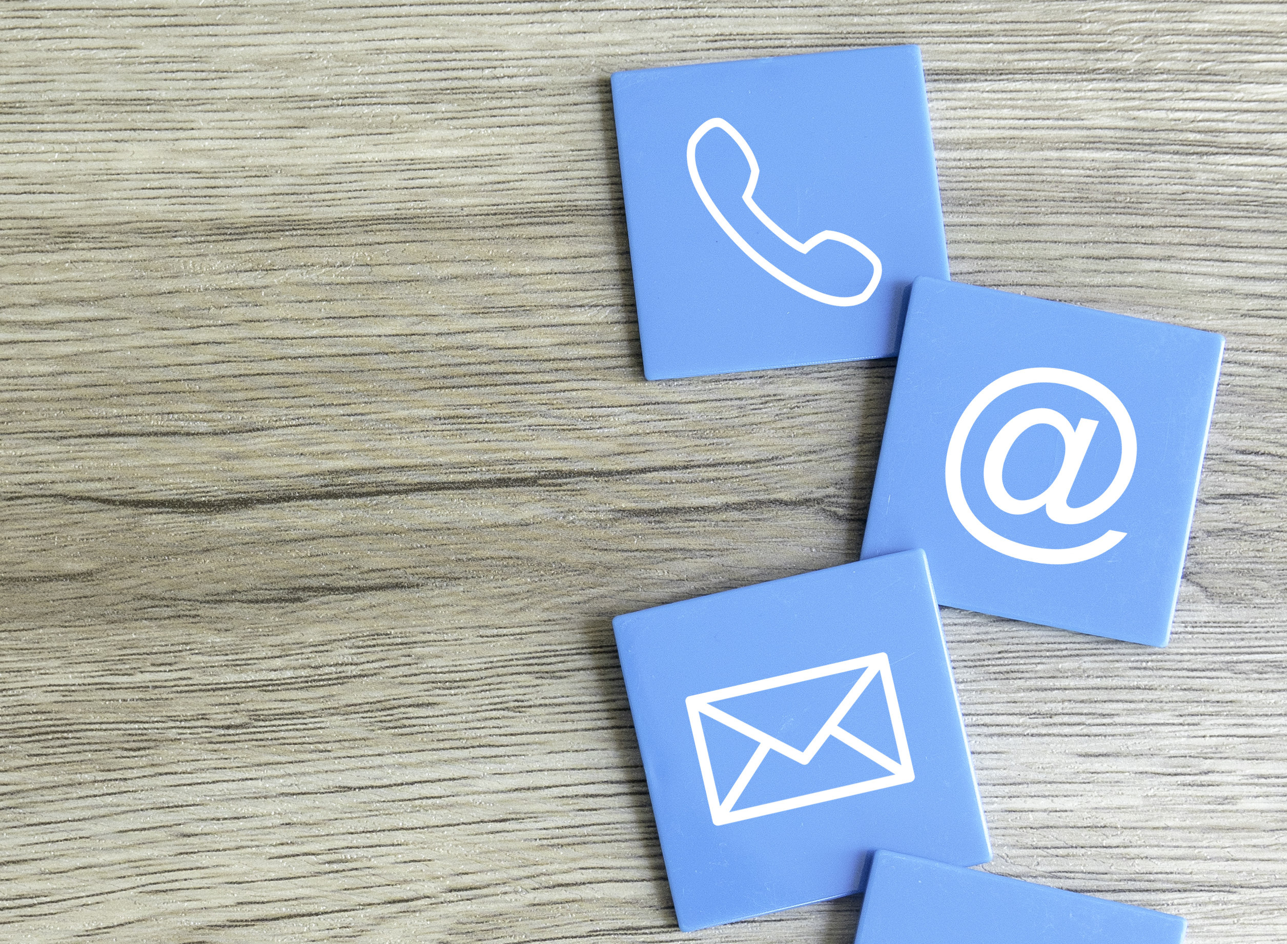 Contact Icons on Wooden Surface Representing Phone, Email, At Symbol, and Chat
