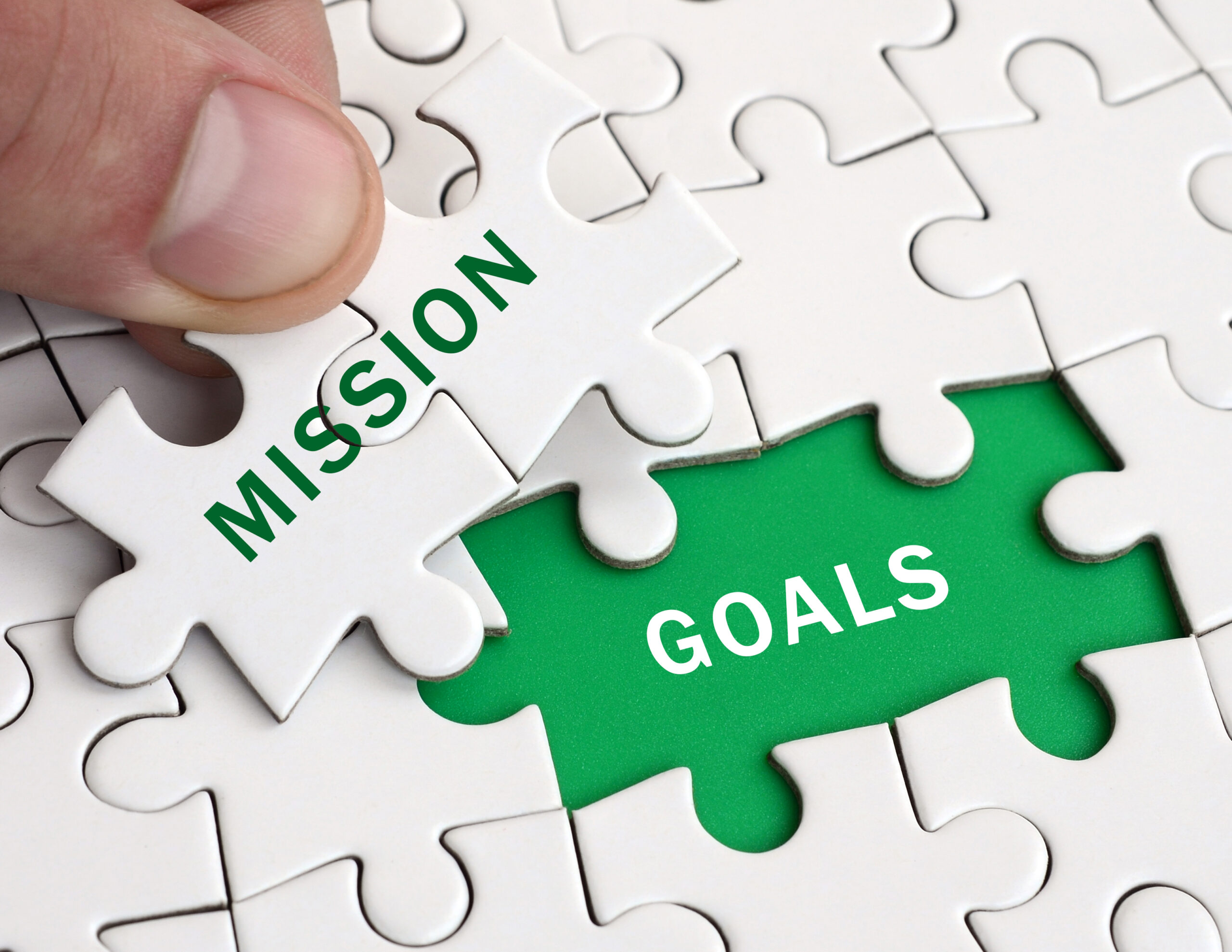 The human hand fills the last missing elements of the surface from the jigsaw puzzle. Image with words mission and goals