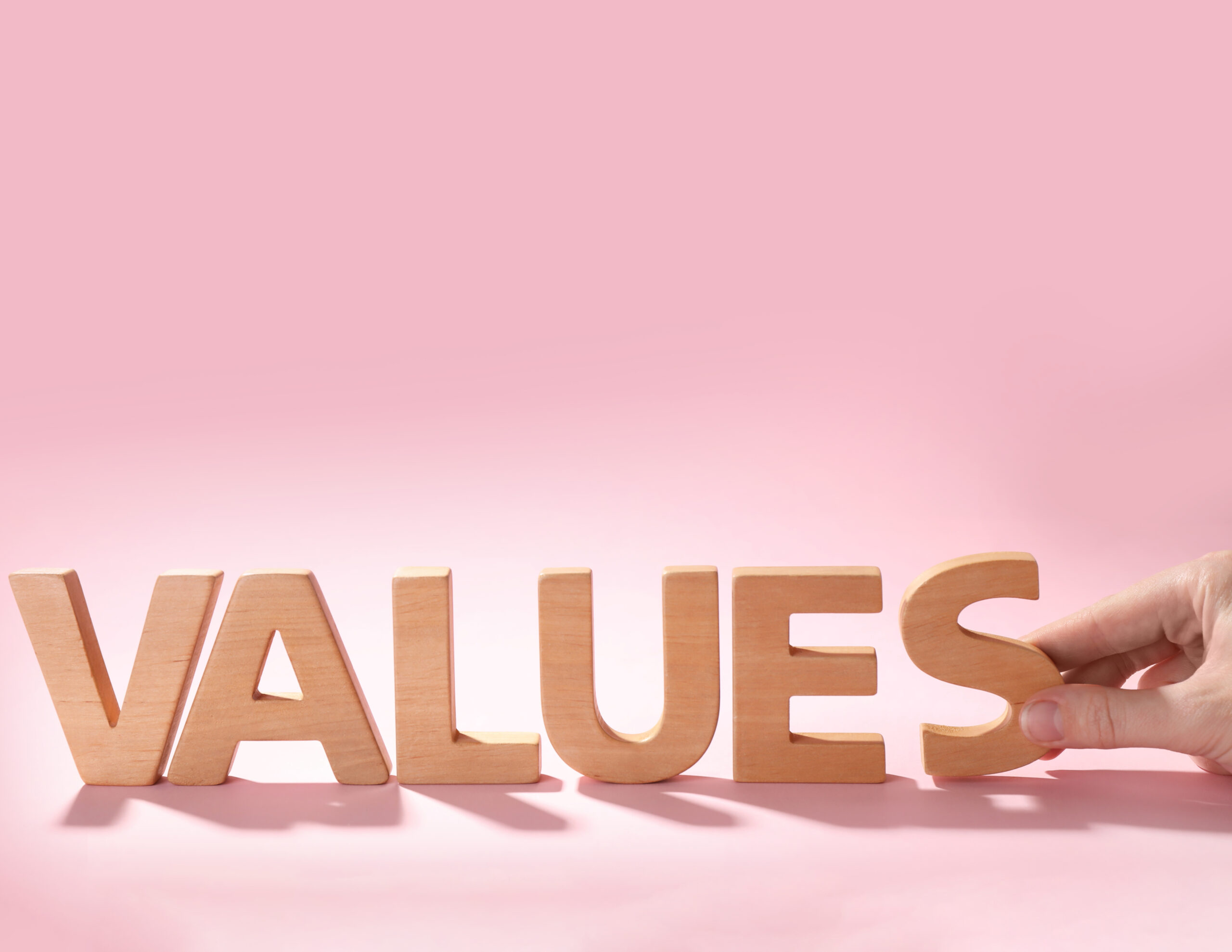 Woman making word VALUES with wooden letters on pink background, closeup