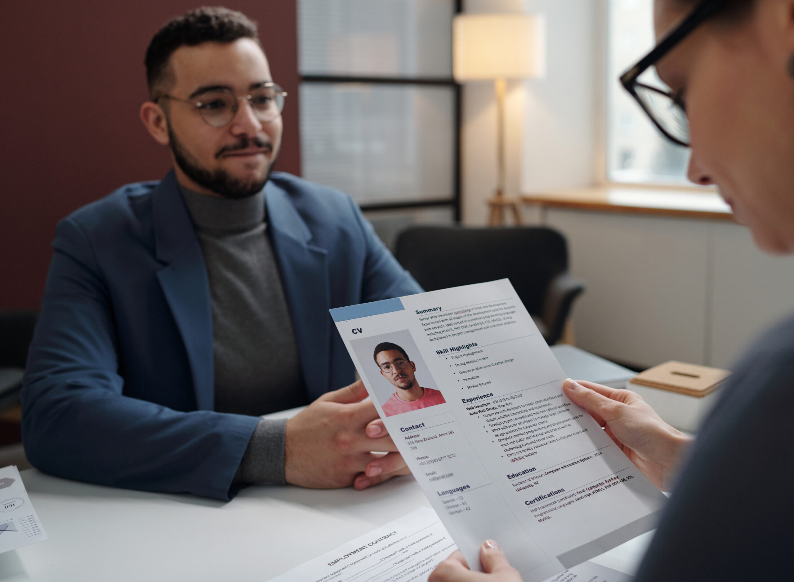 Over shoulder shot of recruiter holding CV during job interview with smiling candidate in defocused background copy space